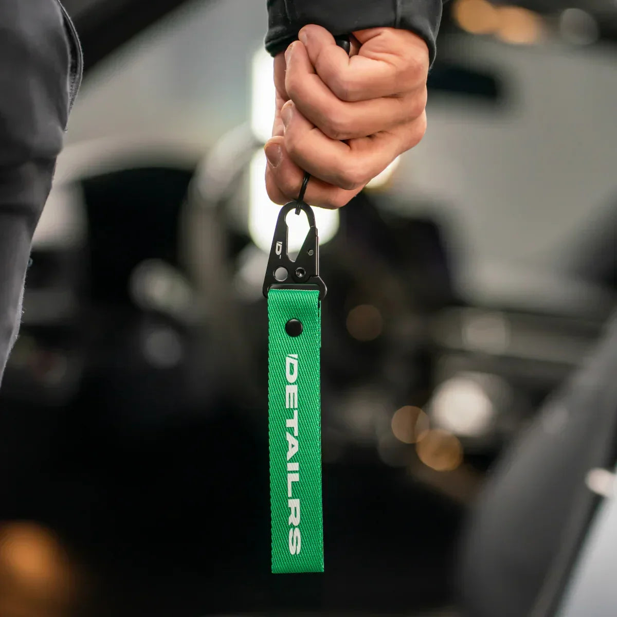 Detailrs sleutelhanger groen met zwarte karabijnhaak gehouden in hand in auto interieur