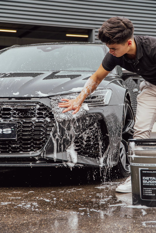 Detailrs Audi RS6 Avant in zwarte kleur wordt met schuim en spons handmatig gewassen door jongeman