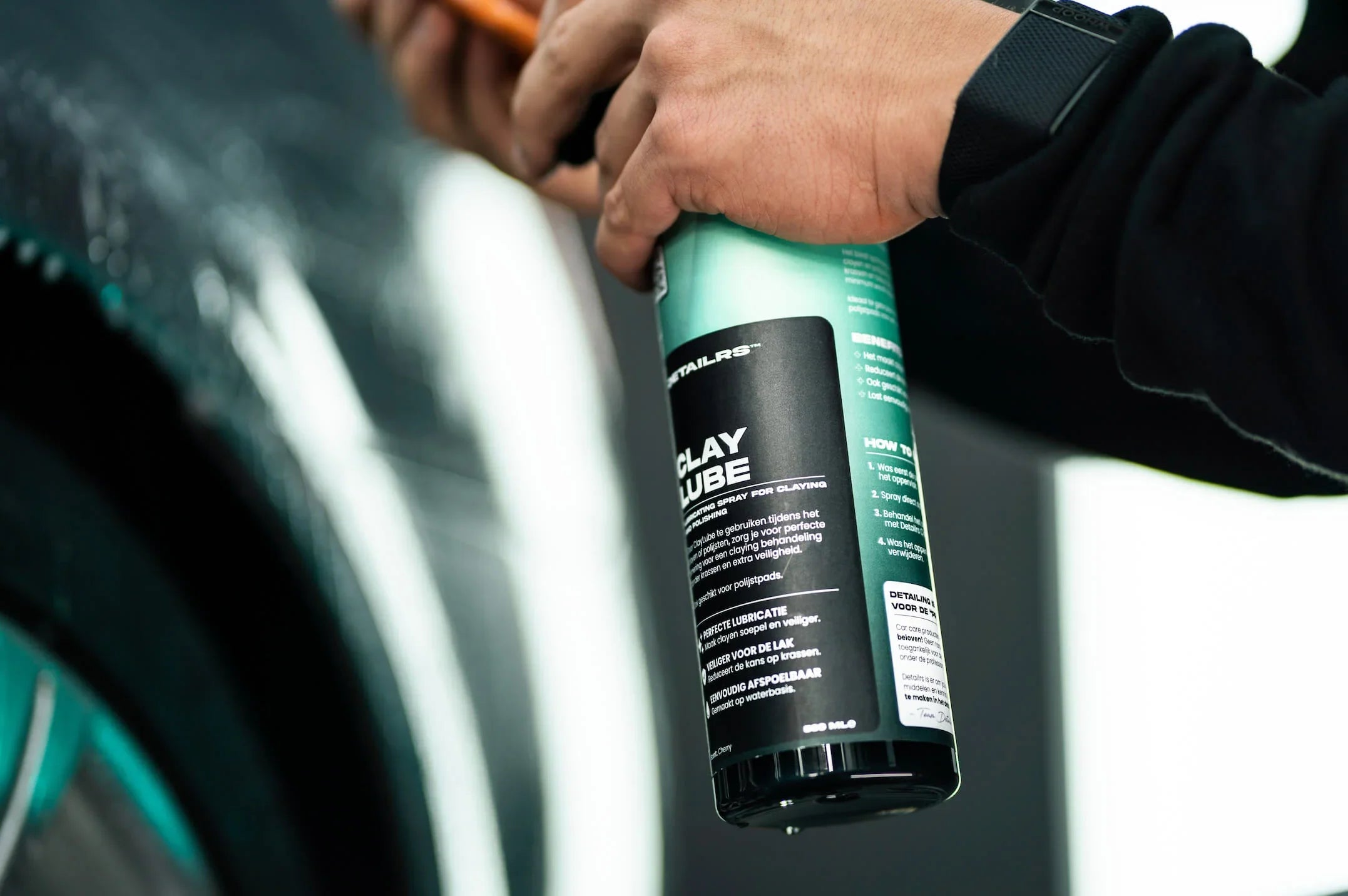 Detailrs Clay Lube spray voor polijsten in handen van persoon naast autovelg