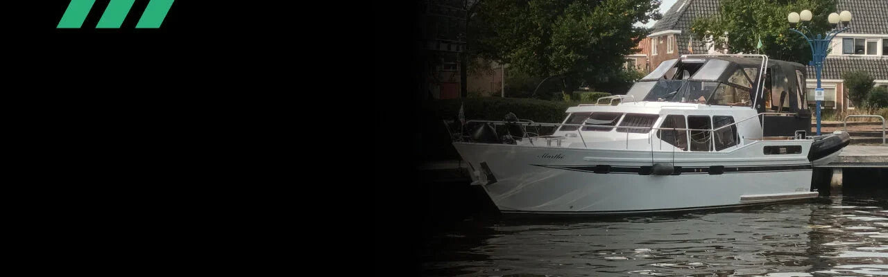 Detailrs luxe wit motorjacht met zwart zonnedek aan kade met huizen en bomen op achtergrond