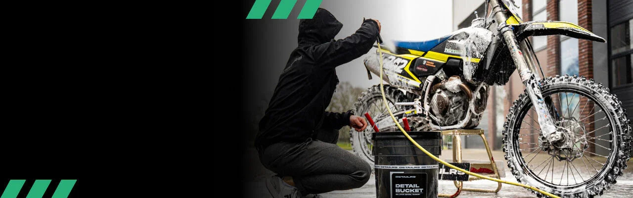 Detailrs Detail Bucket met man in zwarte jas die vuile crossmotor met hogedrukreiniger schoonmaakt