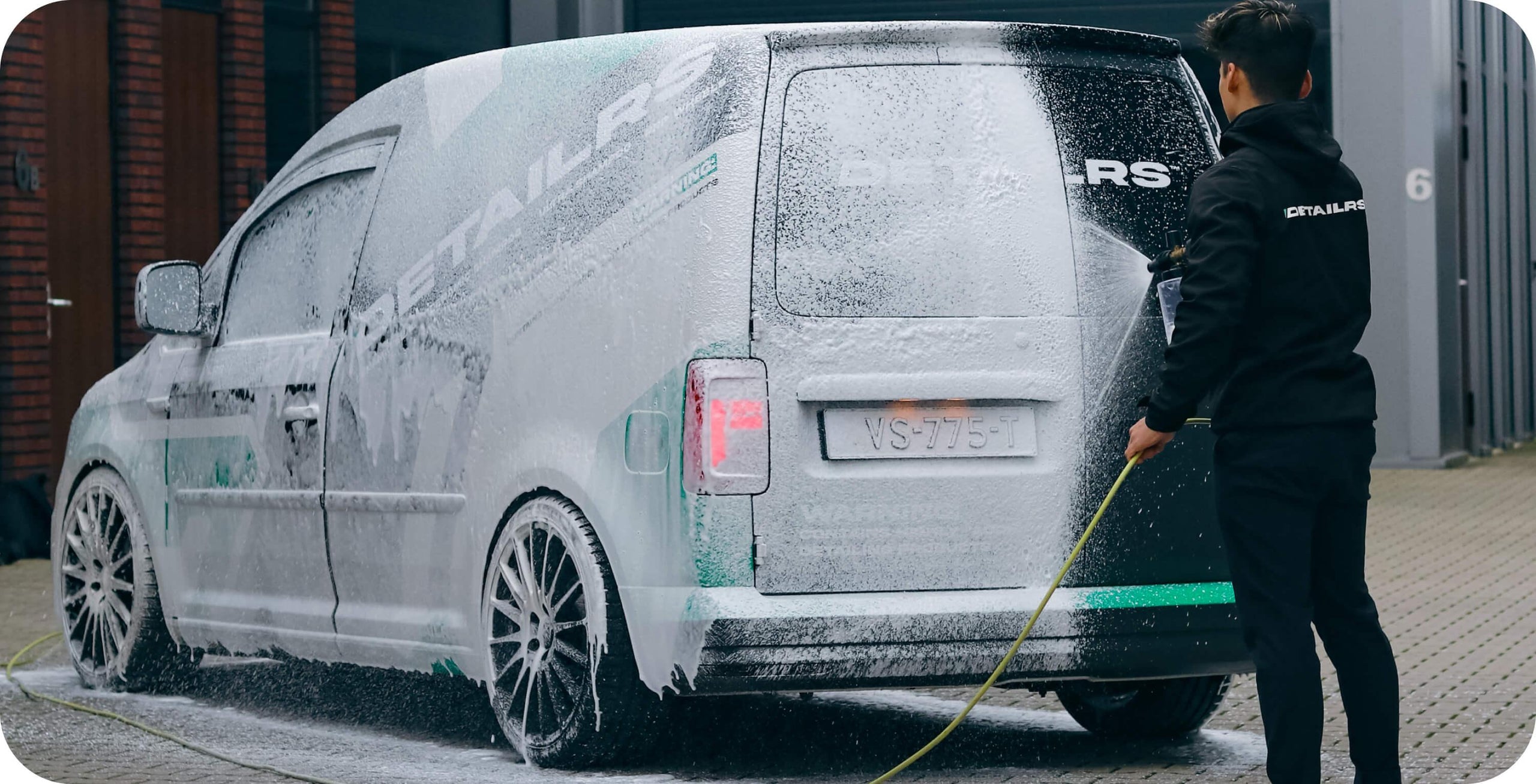 Detailrs snowfoam in schuimverdelende spuit gebruikt door persoon om zwarte bestelauto schoon te maken