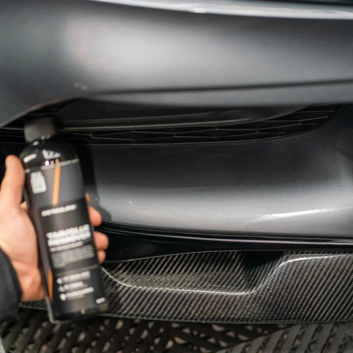 Detailrs Tar and Glue tar remover in hand bij auto met grijze bumper en carbon fiber details