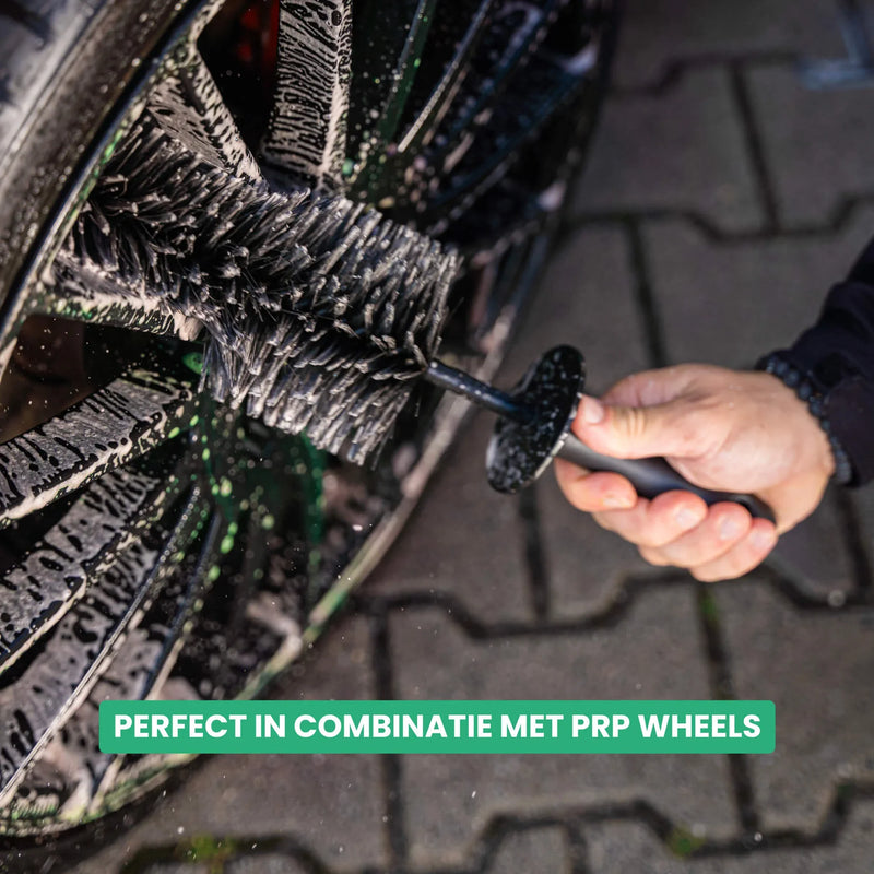 Detailrs wielborstel schoonmaakt auto velg met schuim op straatstenen
