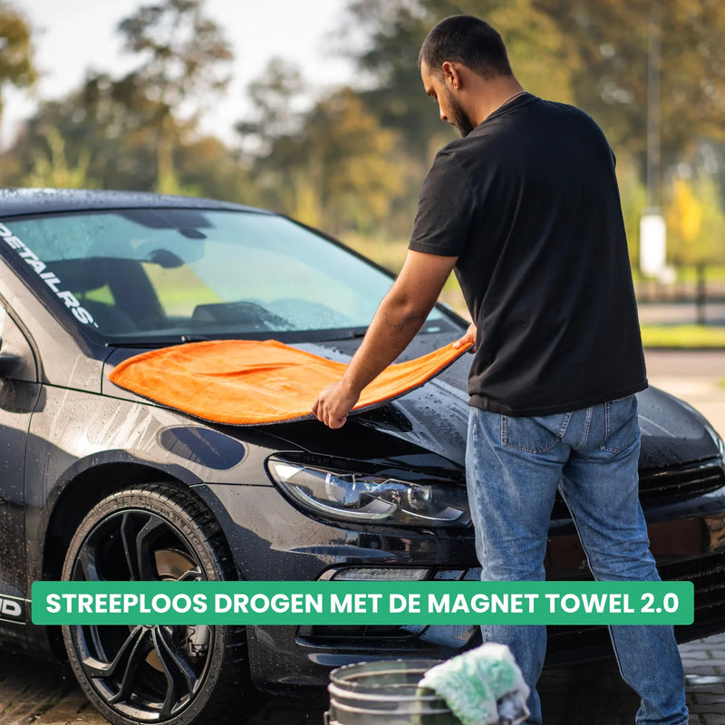 Detailrs Magnet Towel 2.0, man droogt zwarte auto streeploos met oranje microvezel handdoek buiten